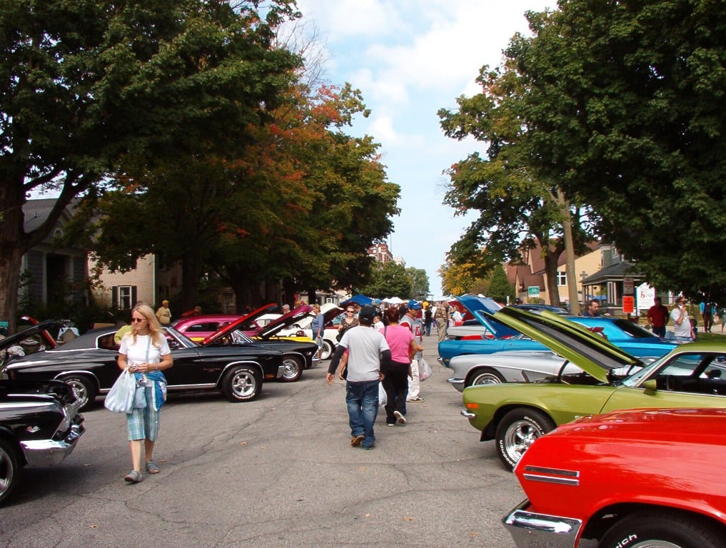 Visitors browsing classic cars parked along a tree-lined street in downtown La Porte