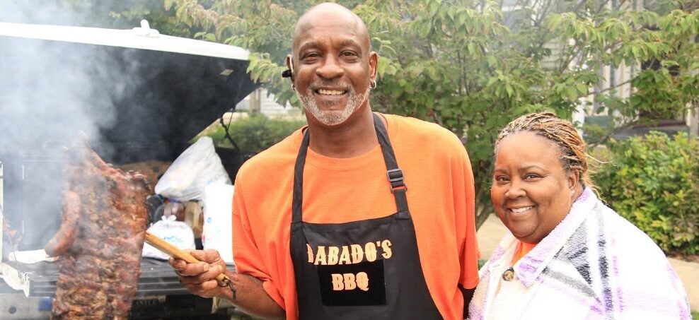 Smiling barbecue vendor in an orange shirt and apron at the La Porte Sunflower Fair